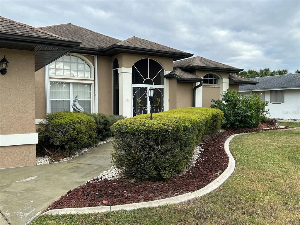 A tan house exterior features a concrete walkway, a manicured hedge, and a front entryway — 1238 YORKSHIRE STREET, PORT CHARLOTTE, FL