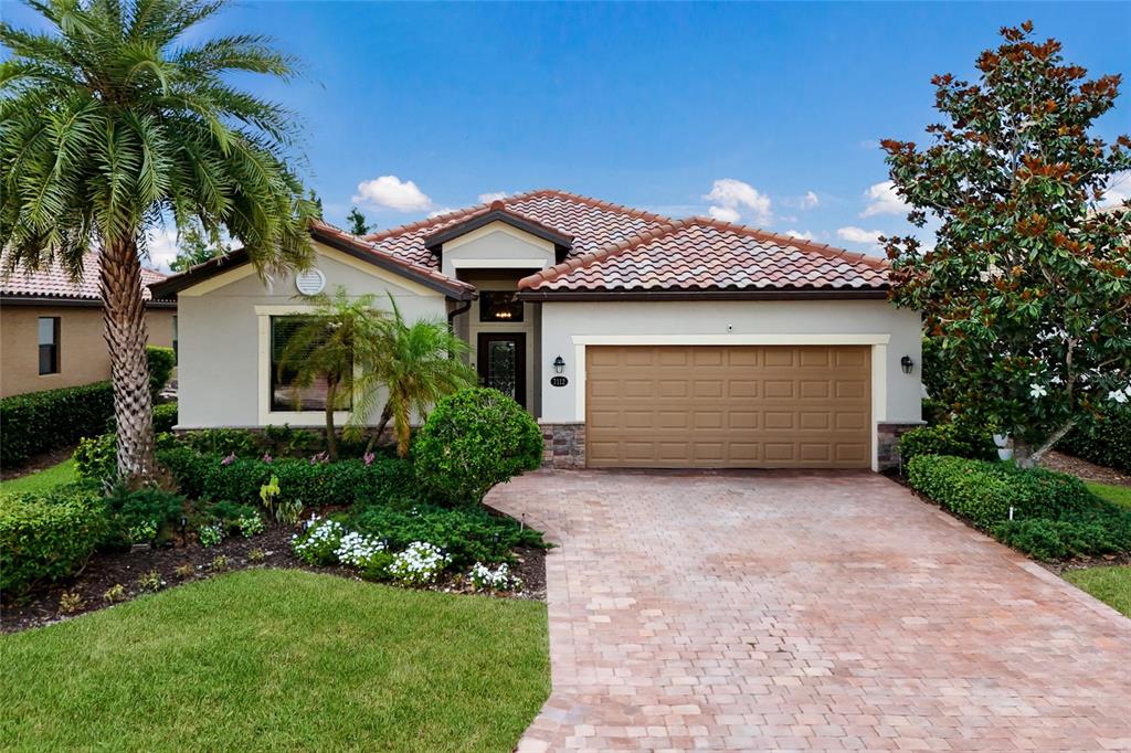 A single-story house with a tiled roof, tan stucco exterior, and a brick paver driveway — 7112 MARSH VIEW TERRACE, BRADENTON, FL