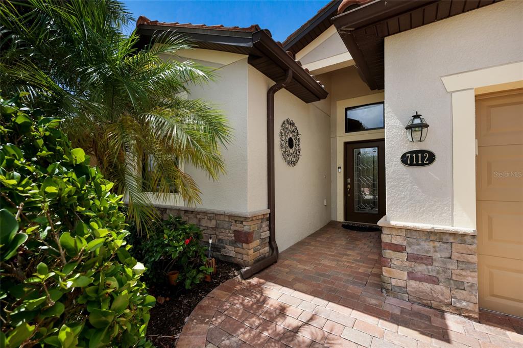 A paved walkway leads to the front entrance of a house with stone accents — 7112 MARSH VIEW TERRACE, BRADENTON, FL
