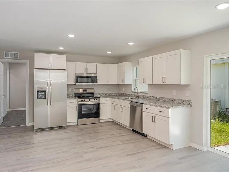 A kitchen with white cabinets, stainless steel appliances, and gray speckled countertops — 308 AVE P NW, WINTER HAVEN, FL