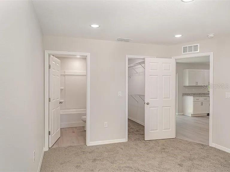 A bedroom with gray carpet features doors leading to a bathroom, closet, and kitchen area — 308 AVE P NW, WINTER HAVEN, FL