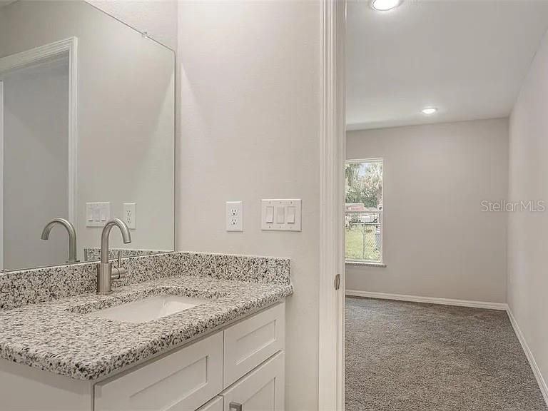 A bathroom vanity with a granite countertop and sink sits next to a carpeted bedroom — 308 AVE P NW, WINTER HAVEN, FL
