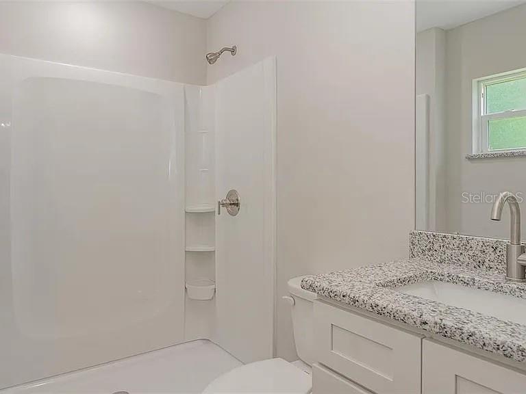 A bathroom features a white shower stall, a granite vanity countertop, and a window — 308 AVE P NW, WINTER HAVEN, FL