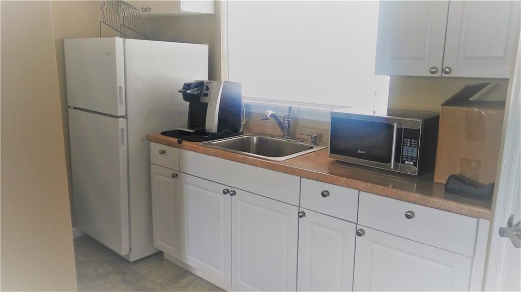 A small kitchen features white cabinets, a stainless steel sink, a microwave, and a refrigerator — 27 SE 24 Avenue # 2, Pompano Beach FL 33062, POMPANO BEACH, FL