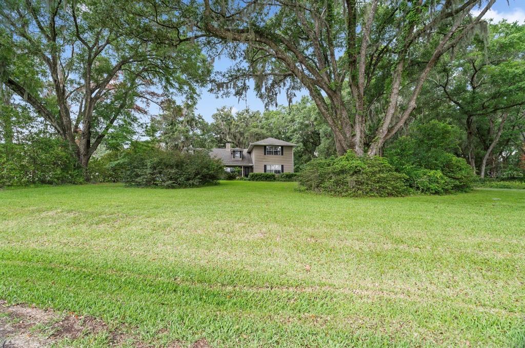 A two-story house with tan siding sits behind a large lawn and mature oak trees — 4370 SE 26TH TERRACE ROAD, OCALA, FL