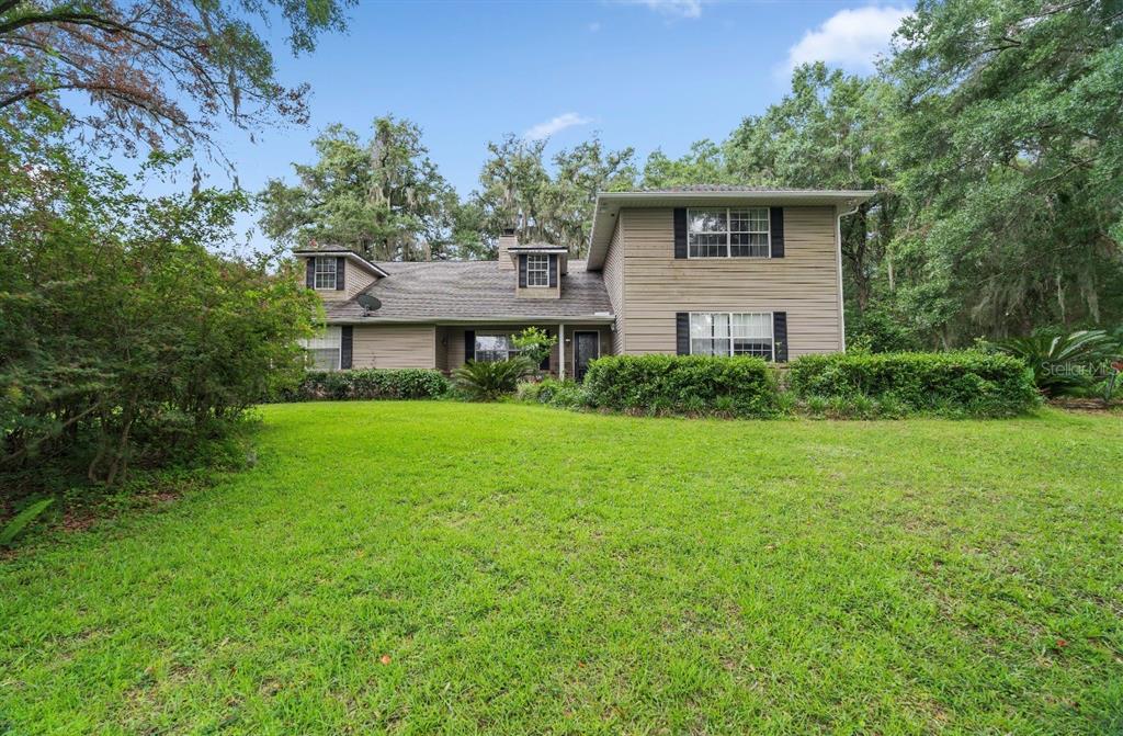 A two-story house with tan siding and a large front lawn surrounded by trees — 4370 SE 26TH TERRACE ROAD, OCALA, FL