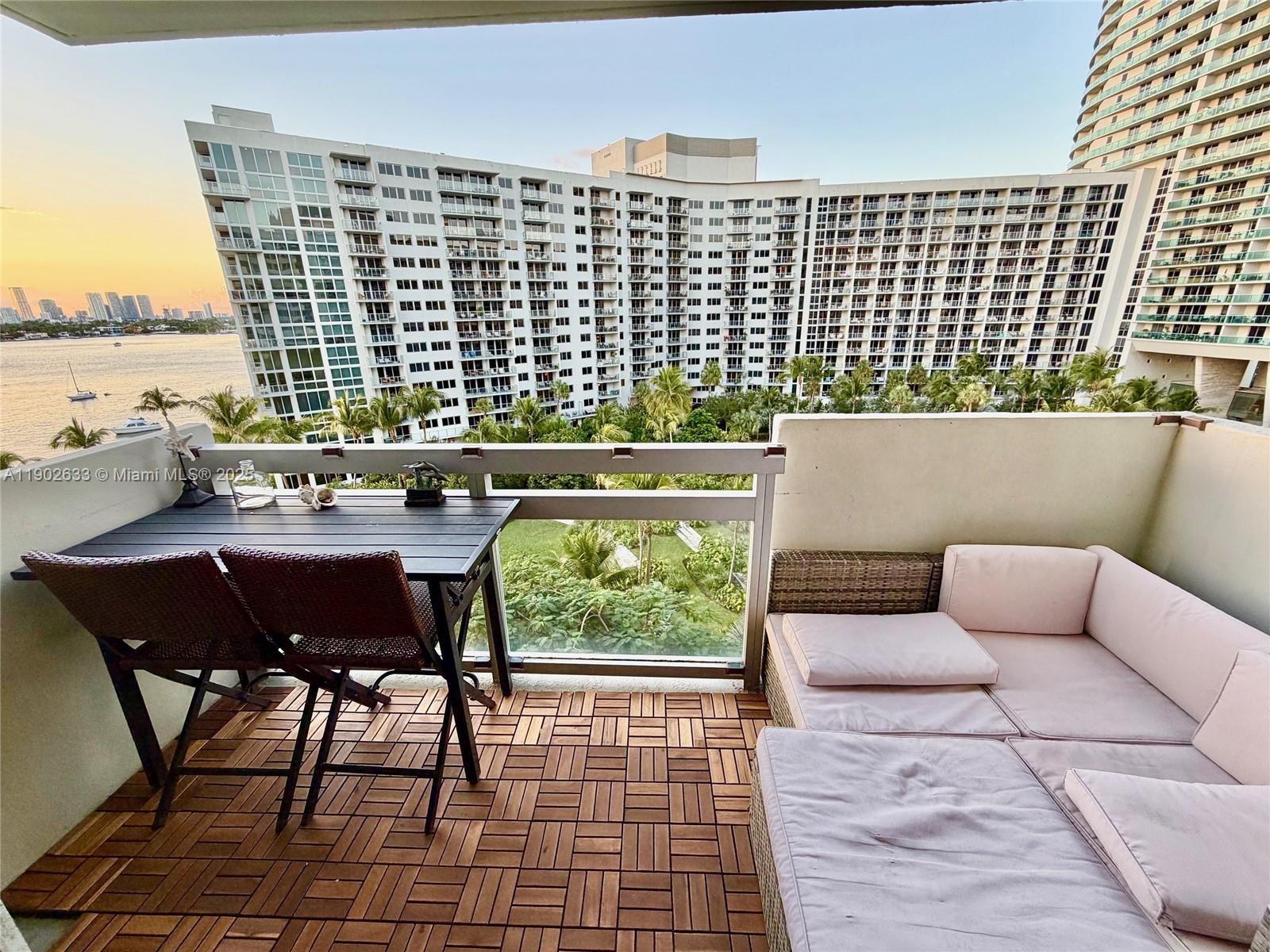 A balcony features a wooden deck, a dining set, and a sectional sofa overlooking water — 1500 Bay Rd # 846S, Miami Beach FL 33139, MIAMI BEACH, FL