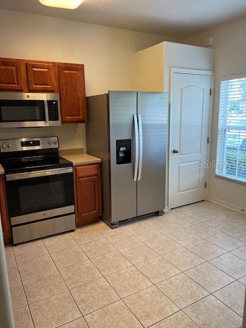 A kitchen features stainless steel appliances, wood cabinets, and light-colored tile flooring — 1140 HILLHURST DRIVE, WESLEY CHAPEL, FL