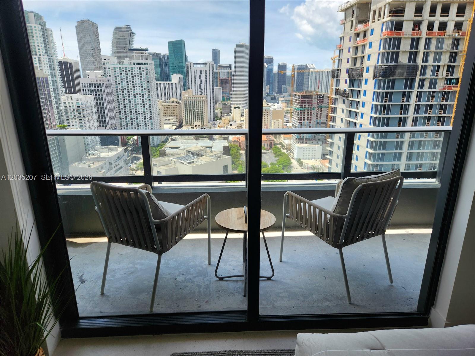 A balcony with two chairs and a small table overlooks a dense city skyline — 601 NE 1 AVE # 2812, Miami FL 33132, MIAMI, FL