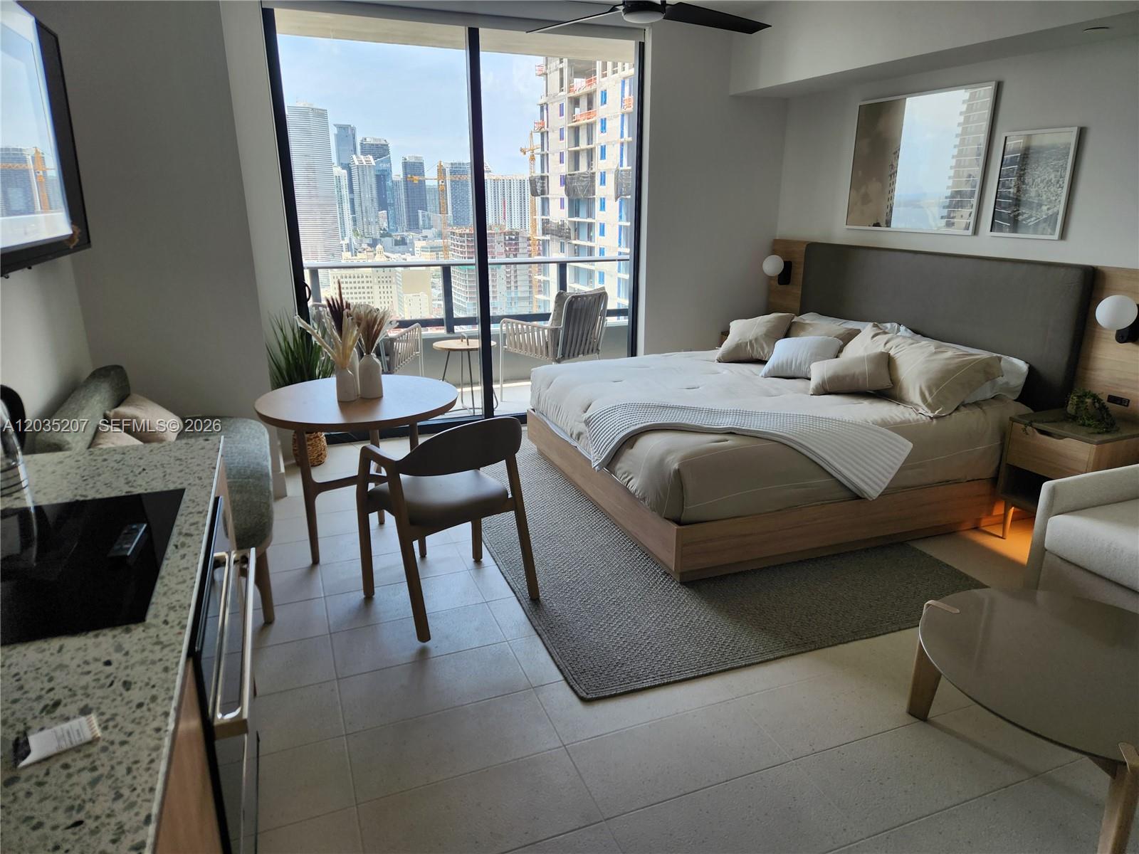 A modern studio apartment features a bed, dining area, and balcony overlooking a city skyline — 601 NE 1 AVE # 2812, Miami FL 33132, MIAMI, FL