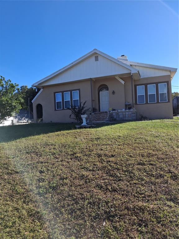 A tan, single-story house with a gabled roof sits on a grassy, sloped lot — 103 GORDON DRIVE, HAINES CITY, FL