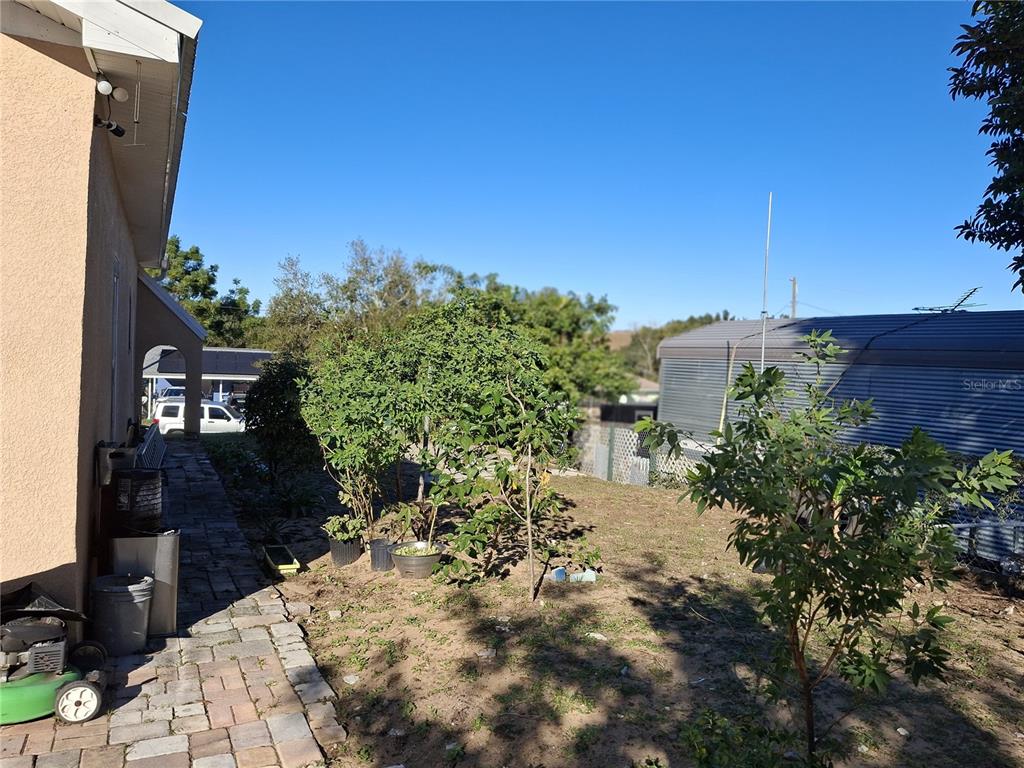 A side yard features a paved walkway, several small trees, and a metal storage structure — 103 GORDON DRIVE, HAINES CITY, FL