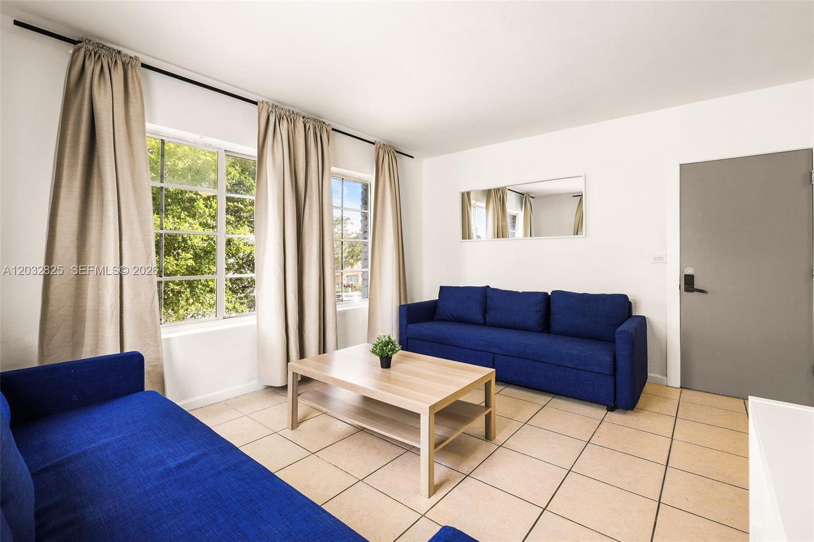 A living room features two blue sofas, a light wood coffee table, and tiled floors — 7340 Harding Ave # 8, Miami Beach FL 33141, MIAMI BEACH, FL