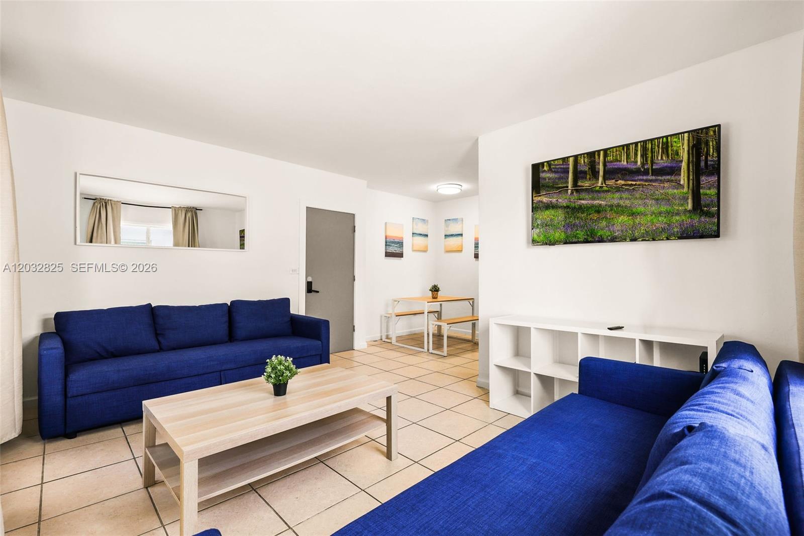 A living room features two blue sofas, a light wood coffee table, and tile flooring — 7340 Harding Ave # 8, Miami Beach FL 33141, MIAMI BEACH, FL