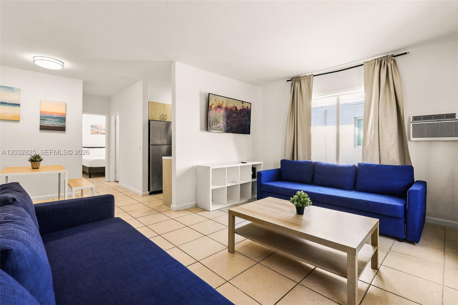 A living room features two blue sofas, a coffee table, and a wall-mounted television — 7340 Harding Ave # 8, Miami Beach FL 33141, MIAMI BEACH, FL
