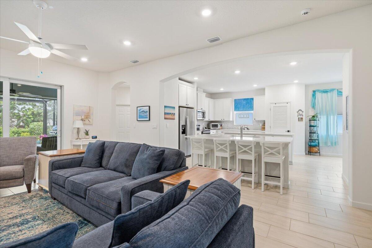A living room with a dark blue sofa opens into a white kitchen with island seating — 31 52nd Square, Vero Beach FL 32968, VERO BEACH, FL