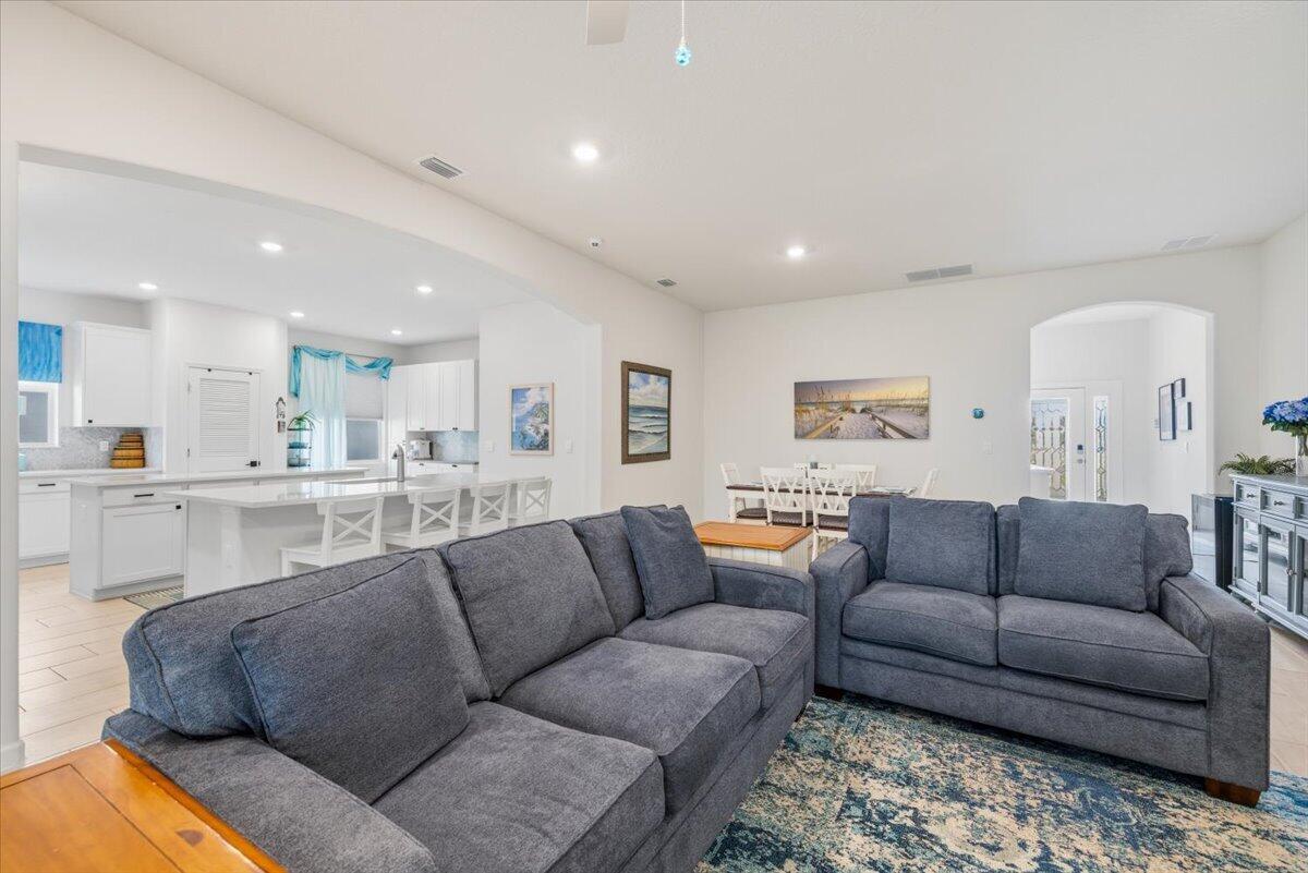 A living room with gray sofas and a patterned rug opens into a white kitchen — 31 52nd Square, Vero Beach FL 32968, VERO BEACH, FL