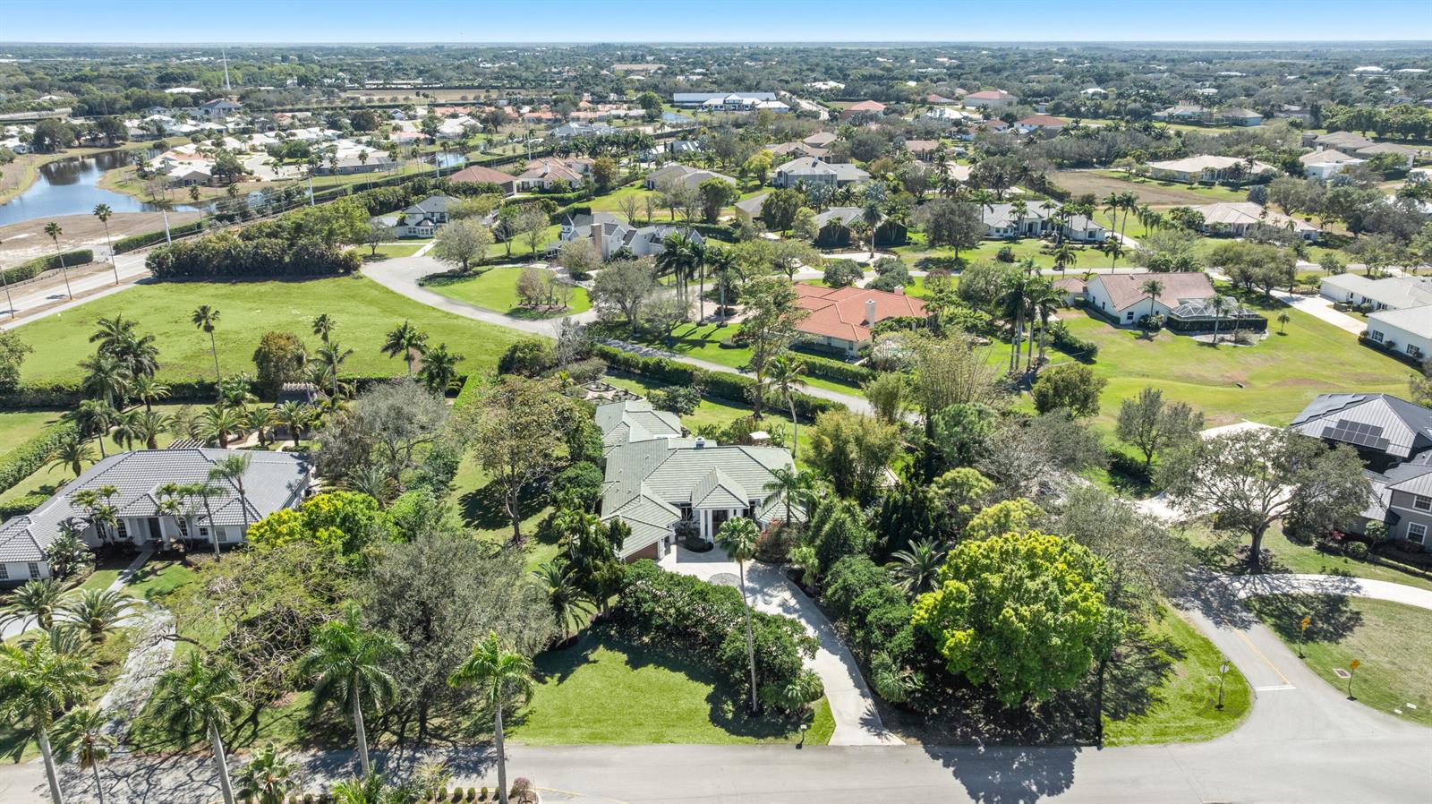 An aerial view shows a single-story house with a green roof surrounded by lush landscaping — 15390 Take Off Place, Wellington FL 33414, WELLINGTON, FL