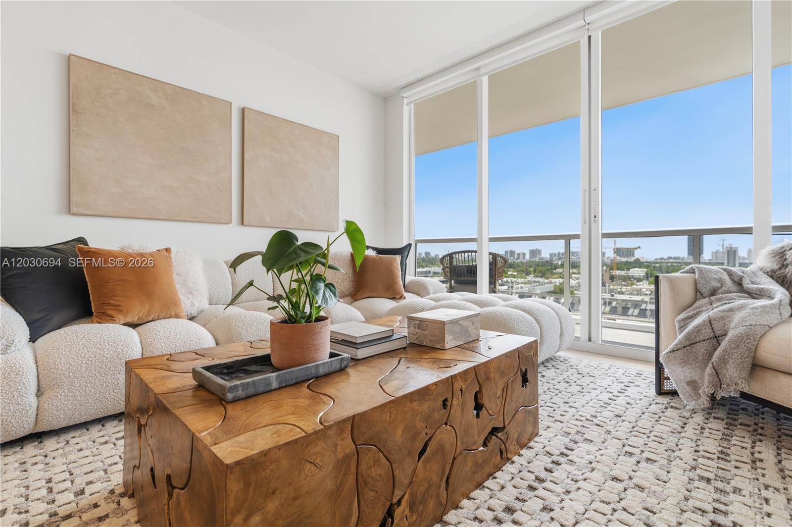 A living room features a textured white sofa, a wooden coffee table, and floor-to-ceiling windows — 1800 Sunset Harbour Dr # 1003, Miami Beach FL 33139, MIAMI BEACH, FL