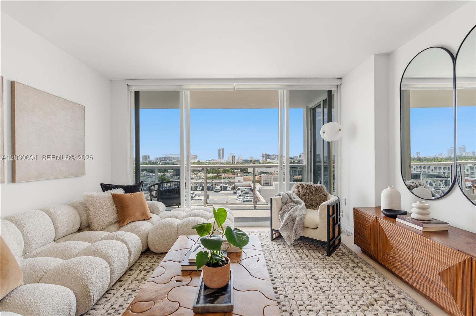 A modern living room features a textured white sofa, wooden coffee table, and balcony view — 1800 Sunset Harbour Dr # 1003, Miami Beach FL 33139, MIAMI BEACH, FL