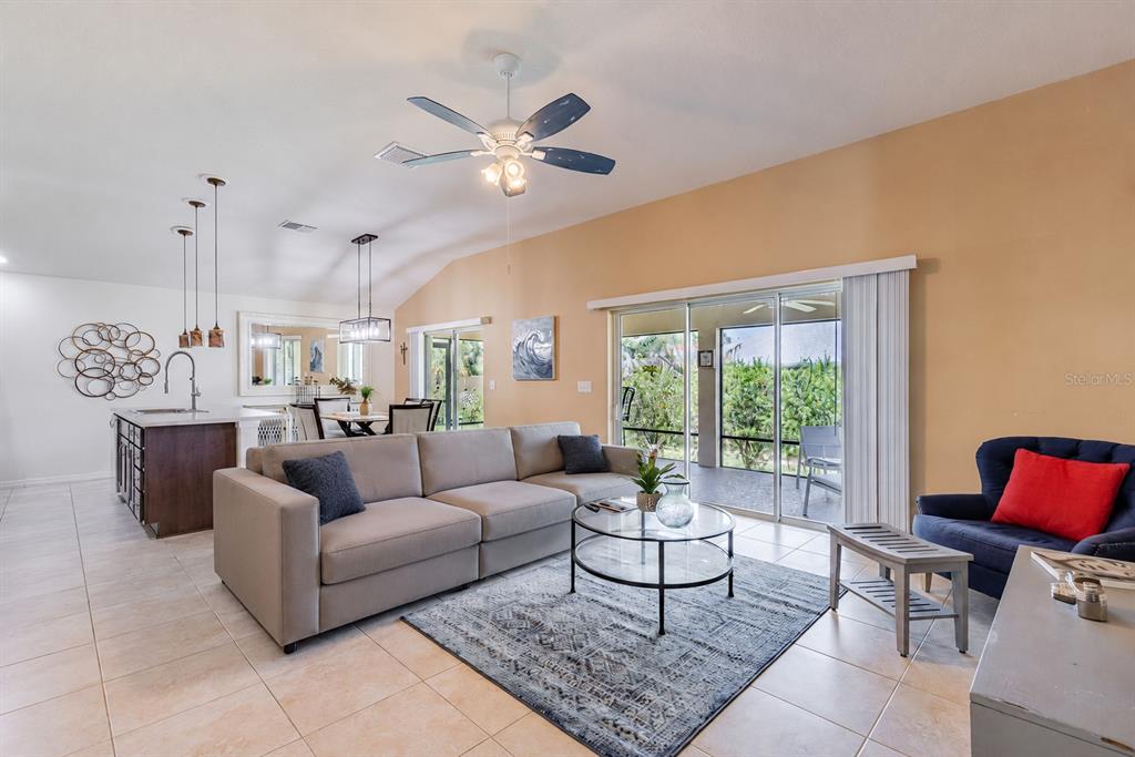 A living room with a beige sofa, glass coffee table, and sliding doors to a patio — 5458 BACON TERRACE, THE VILLAGES, FL