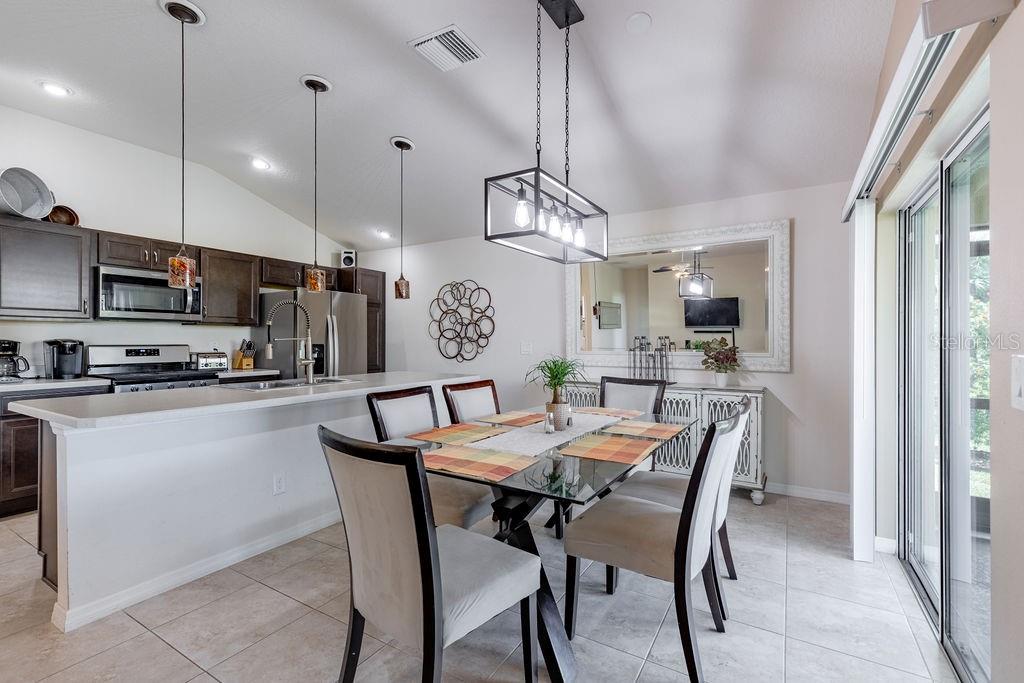 A kitchen with dark cabinets and a breakfast bar overlooks a dining area with seating — 5458 BACON TERRACE, THE VILLAGES, FL