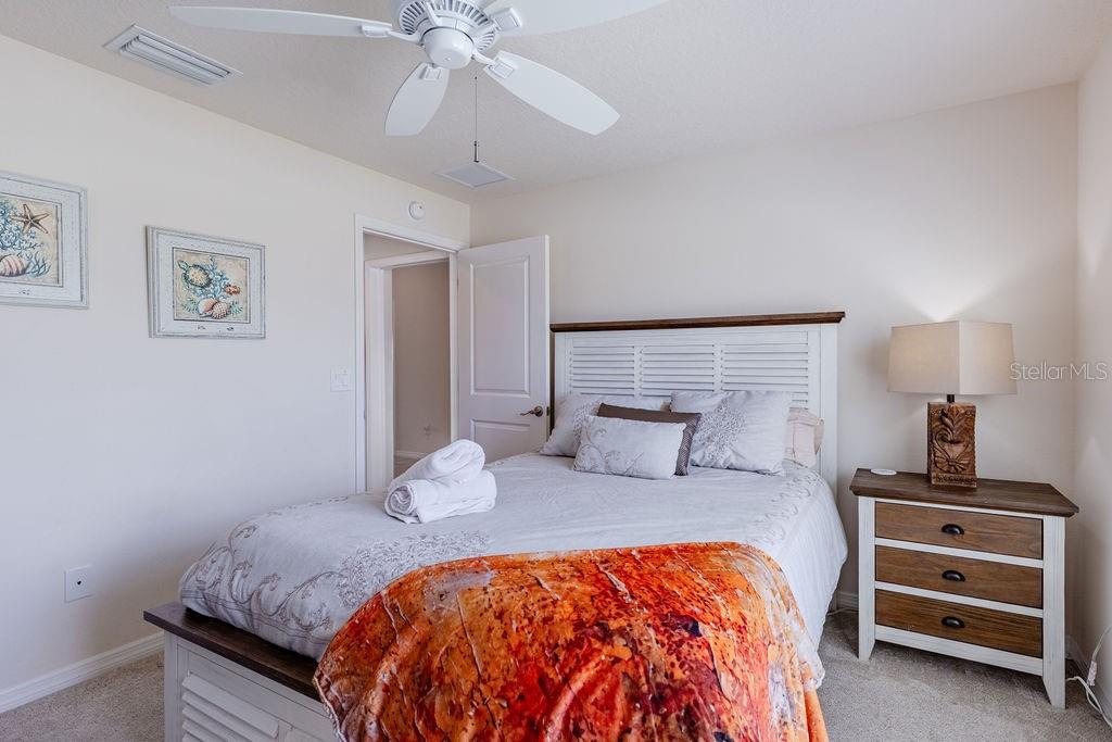 A bedroom features a white bed with a bright orange throw blanket and a nightstand — 5458 BACON TERRACE, THE VILLAGES, FL