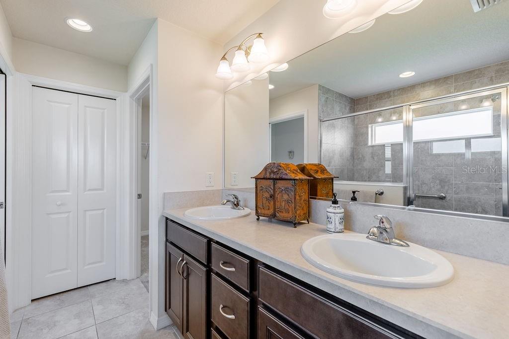A bathroom with a double vanity, dark wood cabinets, light countertops, and a glass-enclosed shower — 5458 BACON TERRACE, THE VILLAGES, FL