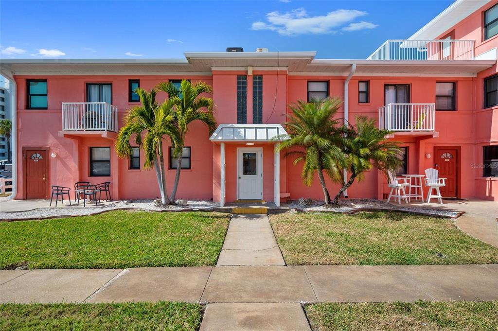A two-story pink building features a central entrance, palm trees, and small balconies — 6800 SUNSET WAY UNIT 106, ST PETE BEACH, FL