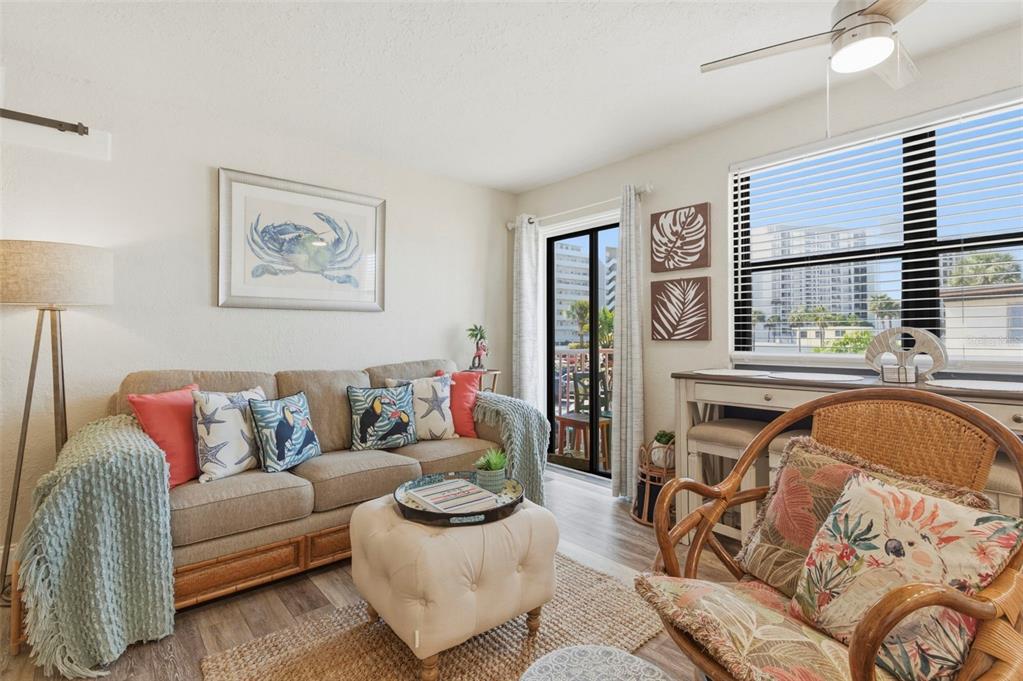 A living room features a beige sofa, a tufted ottoman, and a rattan armchair — 6800 SUNSET WAY UNIT 106, ST PETE BEACH, FL