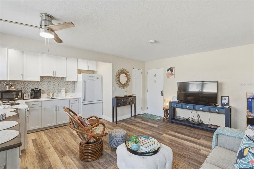 An open-concept living room and kitchen area with light wood flooring and white cabinetry — 6800 SUNSET WAY UNIT 106, ST PETE BEACH, FL