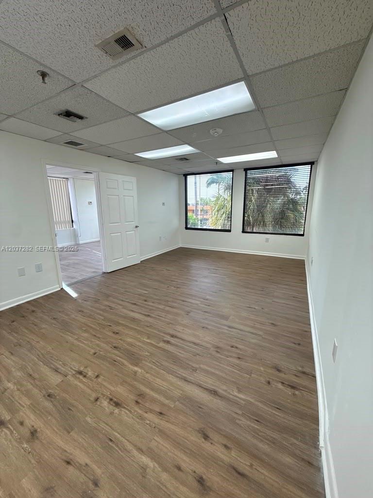 An empty office space features wood-look flooring, a drop ceiling, and two windows with blinds — 2100 W 76th St # 210, Hialeah FL 33016, HIALEAH, FL