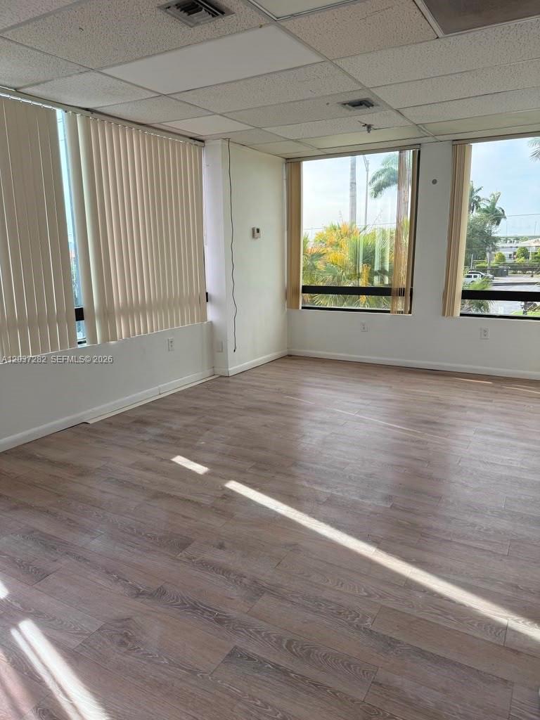 An empty office space features light wood-look flooring, large windows, and a drop ceiling — 2100 W 76th St # 210, Hialeah FL 33016, HIALEAH, FL