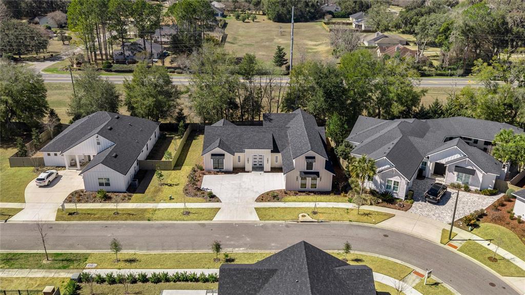 An aerial view shows several modern suburban houses with dark roofs and light-colored exteriors — 1044 SW 120TH DRIVE, GAINESVILLE, FL
