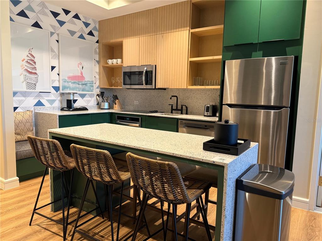 A modern kitchen features green cabinets, light wood accents, a speckled island, and wicker barstools — 3151 SUNSET WALK DRIVE UNIT 302, KISSIMMEE, FL