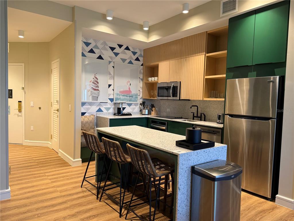 A kitchen features green cabinets, a speckled island with bar stools, and geometric wallpaper — 3151 SUNSET WALK DRIVE UNIT 302, KISSIMMEE, FL