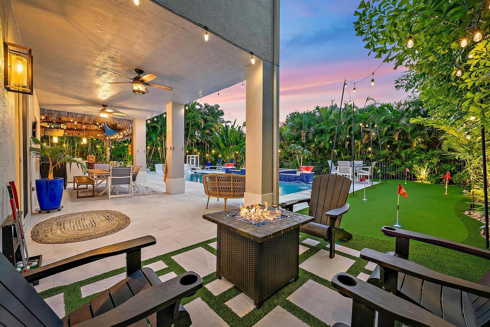A covered patio features a fire pit, seating, and an adjacent putting green with a pool — 152 Porgee Rock Place, Jupiter FL 33458, JUPITER, FL
