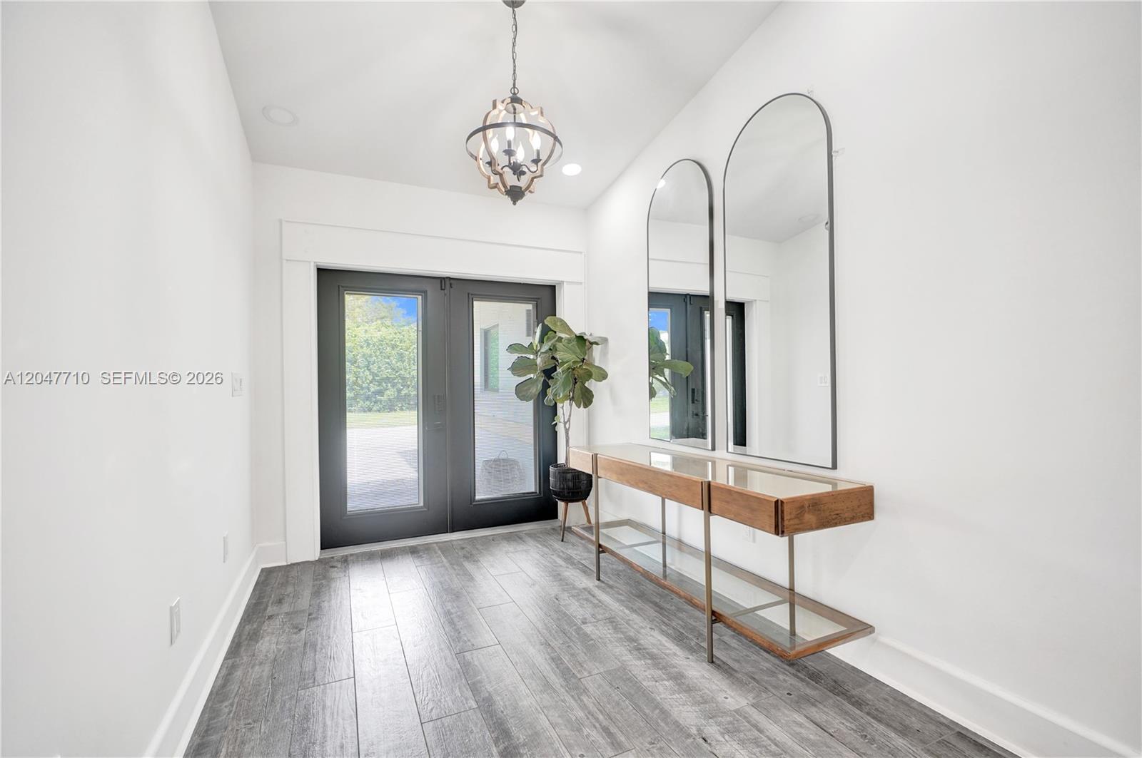 A bright entryway features gray wood-look flooring, a modern chandelier, and two arched wall mirrors — 22421 SW 184th Ave, Miami FL 33170, MIAMI, FL