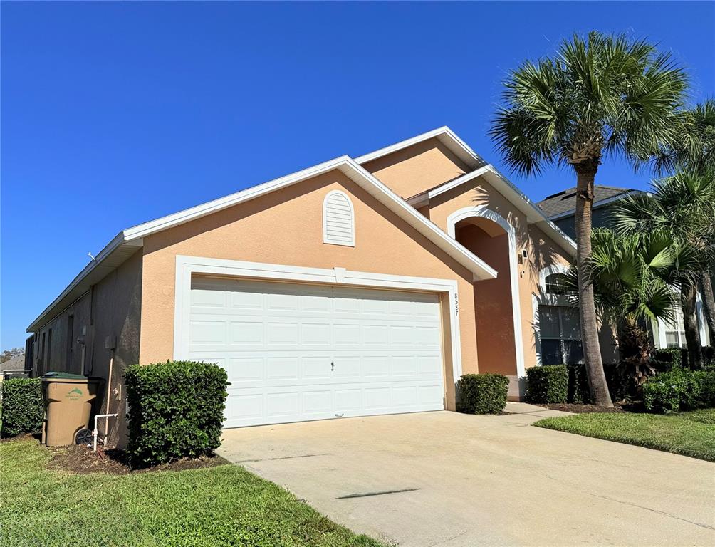 A tan single-story house with a two-car garage and a palm tree in the front — 8587 SUNRISE KEY DRIVE, KISSIMMEE, FL