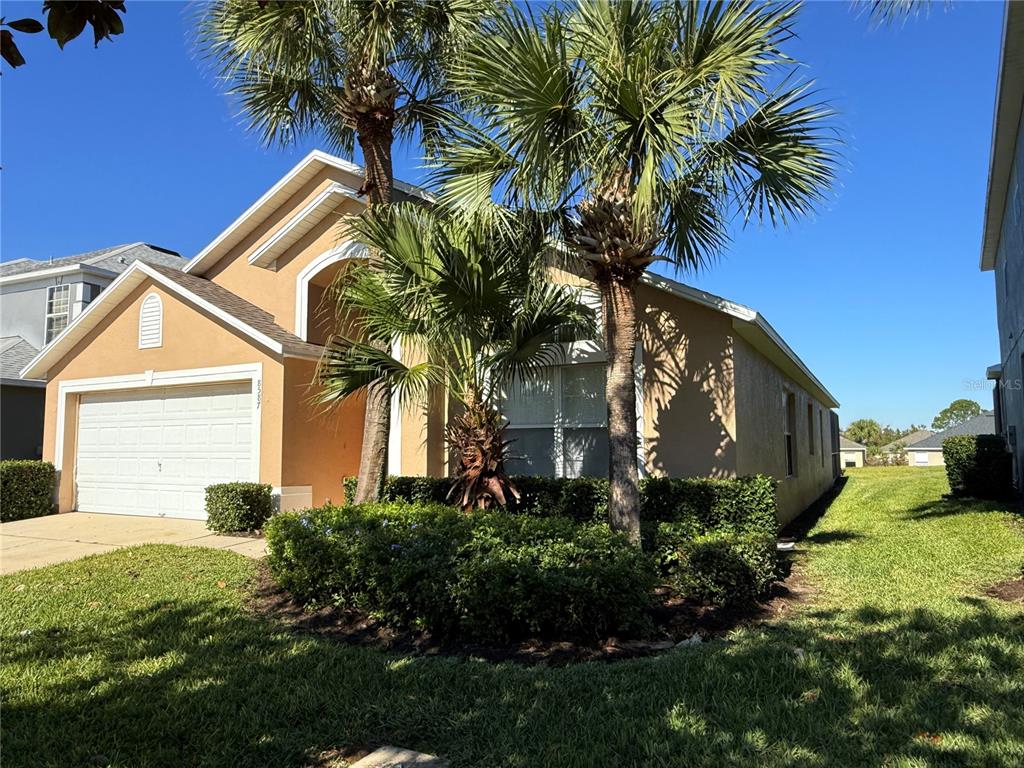 A tan, single-story suburban house features a two-car garage and palm trees in the front — 8587 SUNRISE KEY DRIVE, KISSIMMEE, FL