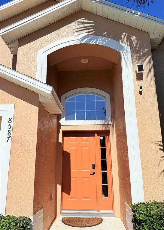 The exterior of a house features an orange front door with a side window — 8587 SUNRISE KEY DRIVE, KISSIMMEE, FL