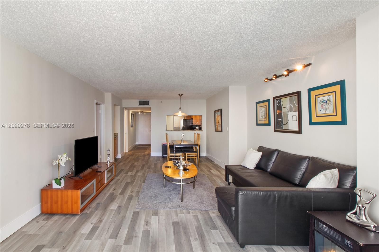 A living room features wood-look flooring, a black leather sofa, and a dining area beyond — 1717 N Bayshore Dr # 2837, Miami FL 33132, MIAMI, FL
