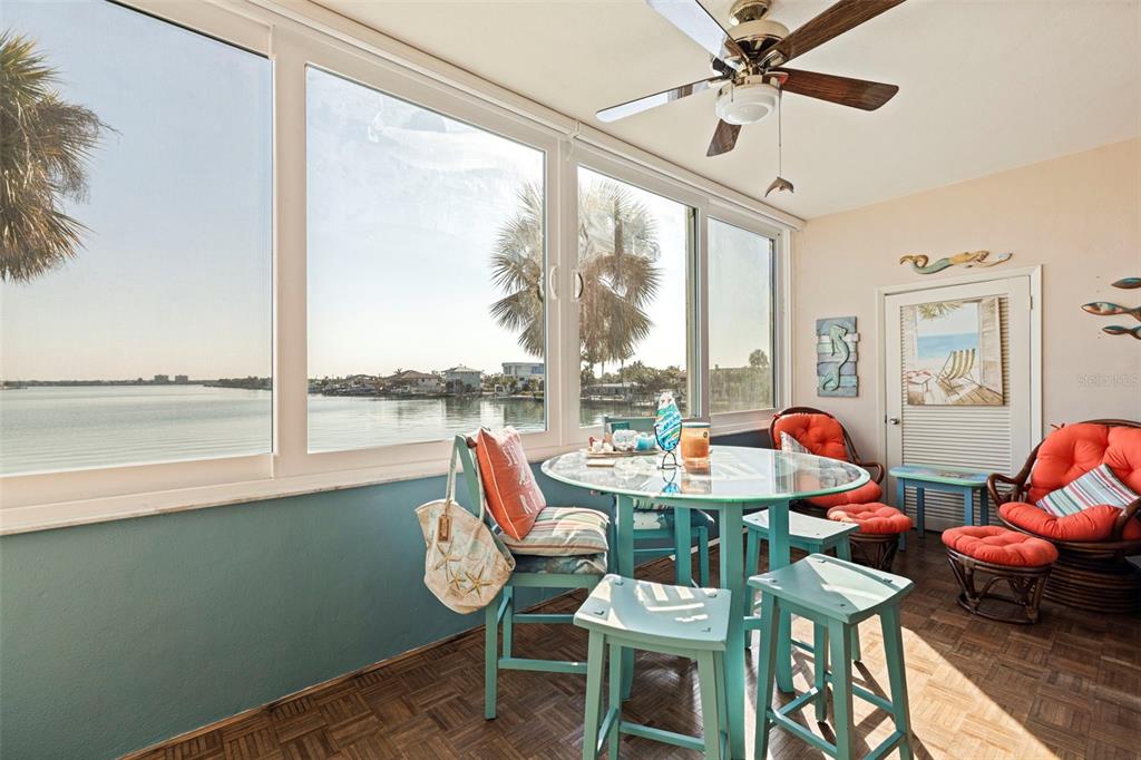 A sunroom with a glass table, wicker chairs, and large windows overlooking a waterfront view — 5555 GULF BOULEVARD UNIT 215, ST PETE BEACH, FL