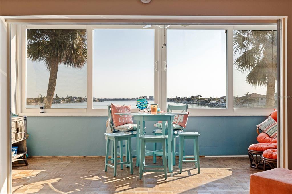 A sunroom with a dining set, parquet flooring, and large windows overlooking a waterfront view — 5555 GULF BOULEVARD UNIT 215, ST PETE BEACH, FL