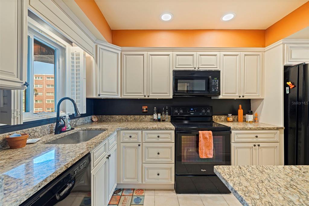 A kitchen features white cabinets, granite countertops, a black stove, and orange wall paint — 5555 GULF BOULEVARD UNIT 215, ST PETE BEACH, FL