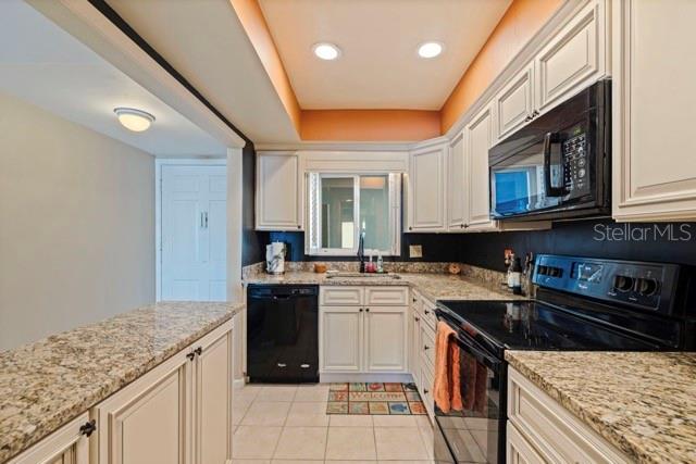 A kitchen features white cabinets, granite countertops, black appliances, and a tiled floor — 5555 GULF BOULEVARD UNIT 215, ST PETE BEACH, FL