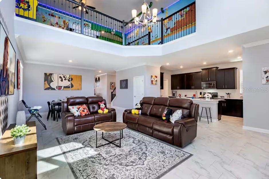 An open-concept living room and kitchen featuring brown leather sofas and a lofted balcony — 4266 PARAGRAPH DRIVE, KISSIMMEE, FL
