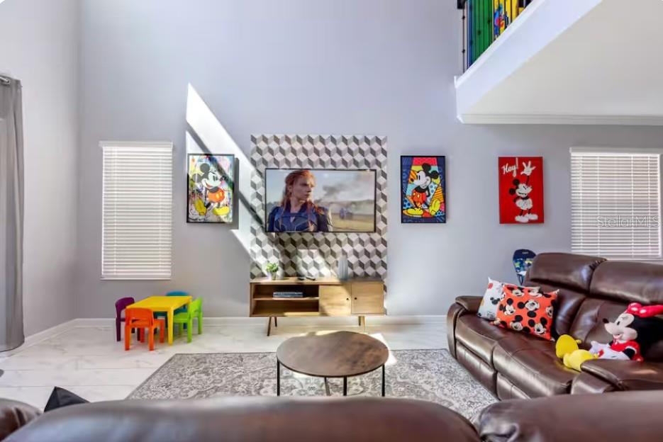 A living room features high ceilings, a geometric accent wall, and Disney-themed decor — 4266 PARAGRAPH DRIVE, KISSIMMEE, FL