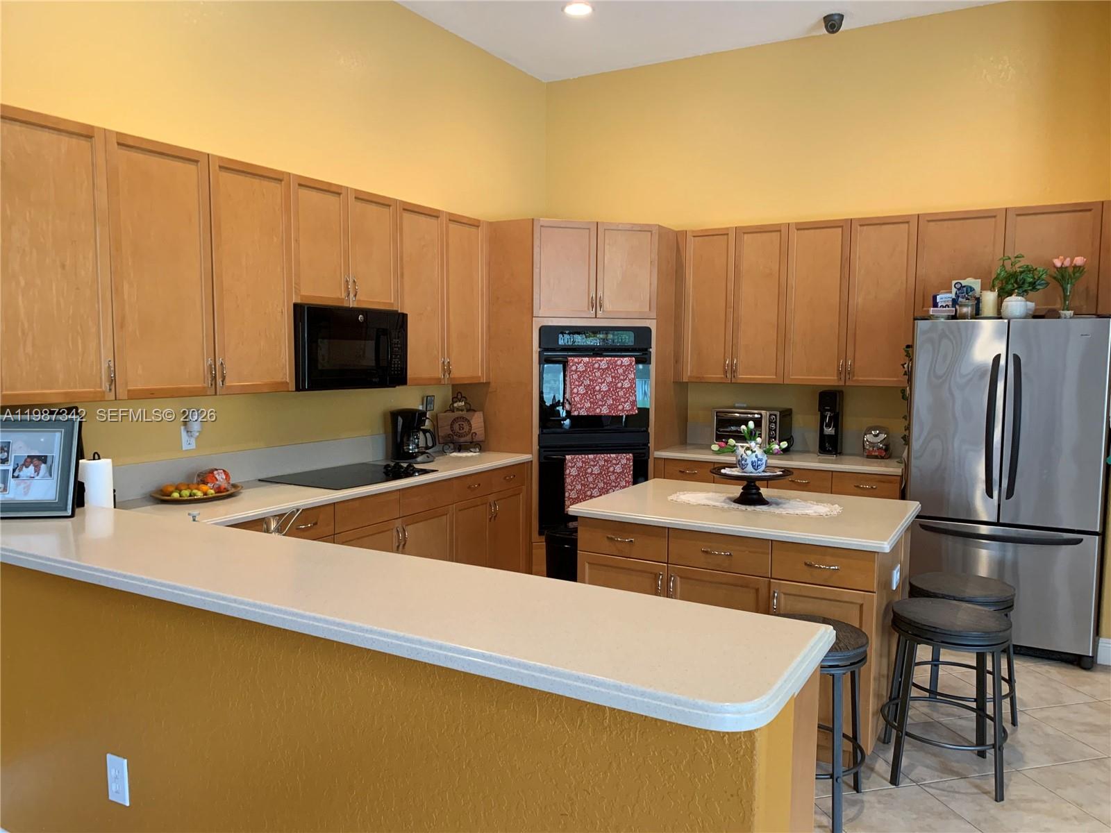 A kitchen features light wood cabinets, stainless steel appliances, a central island, and yellow walls — 4723 SW 195th Way, Miramar FL 33029, MIRAMAR, FL