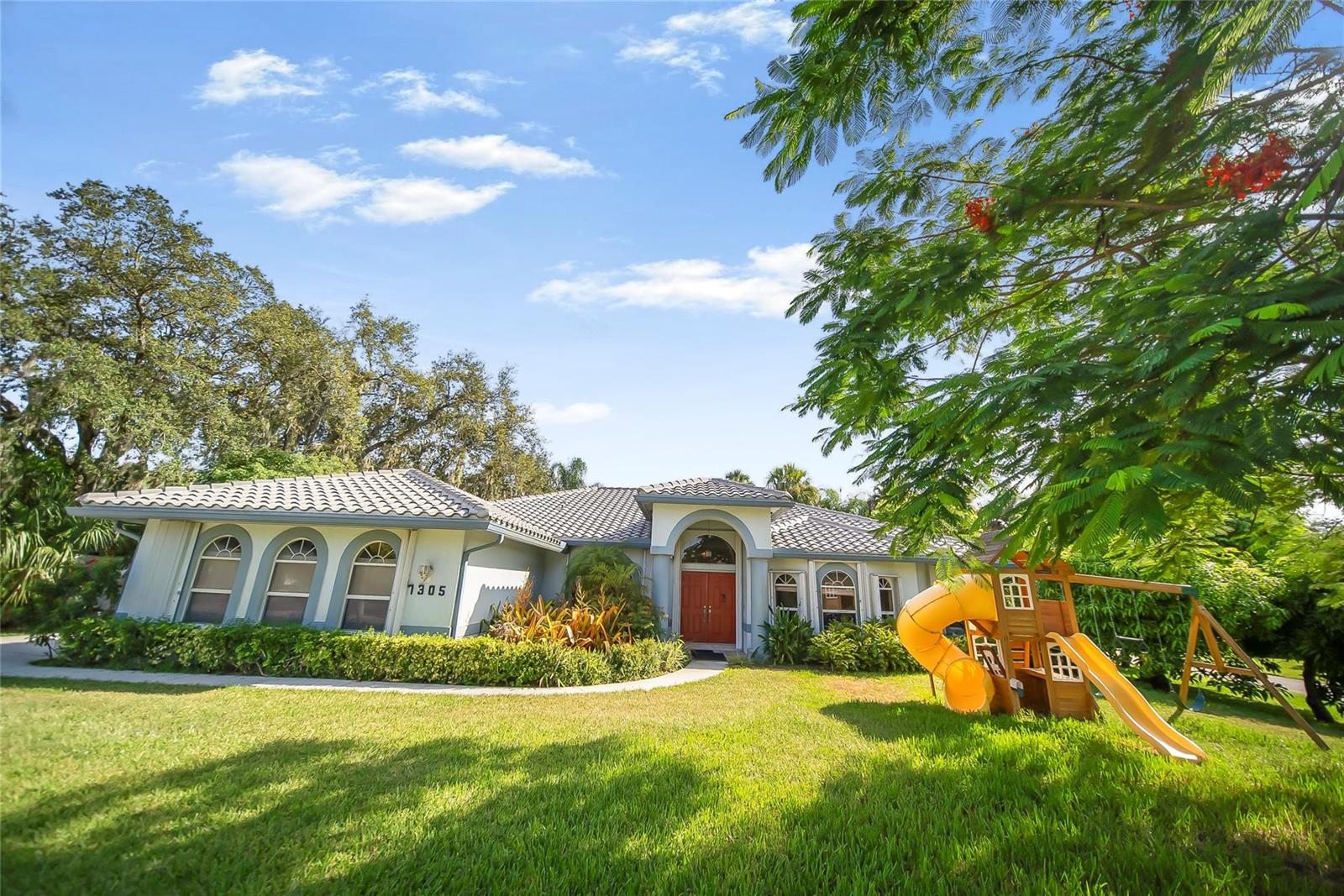 A single-story house with a tiled roof, red front door, and a wooden playground set — 7305 E Elyse Circle, Port St. Lucie FL 34952, PORT ST. LUCIE, FL